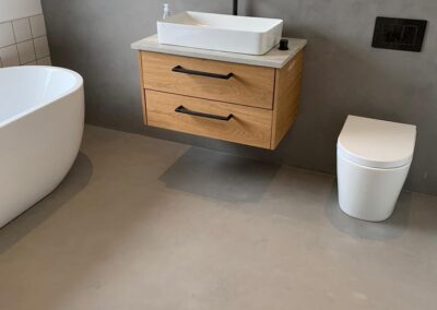 Baño moderno con revestimiento gris, bañera blanca y mueble de lavabo suspendido de madera